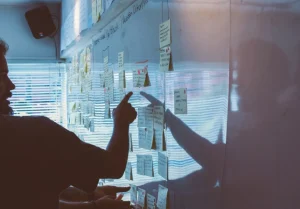 A member of a marketing communications team pointing at a white board of Post-its discussing planning, communications strategy, internal communications, external communications, and Communications Development and Deployment.